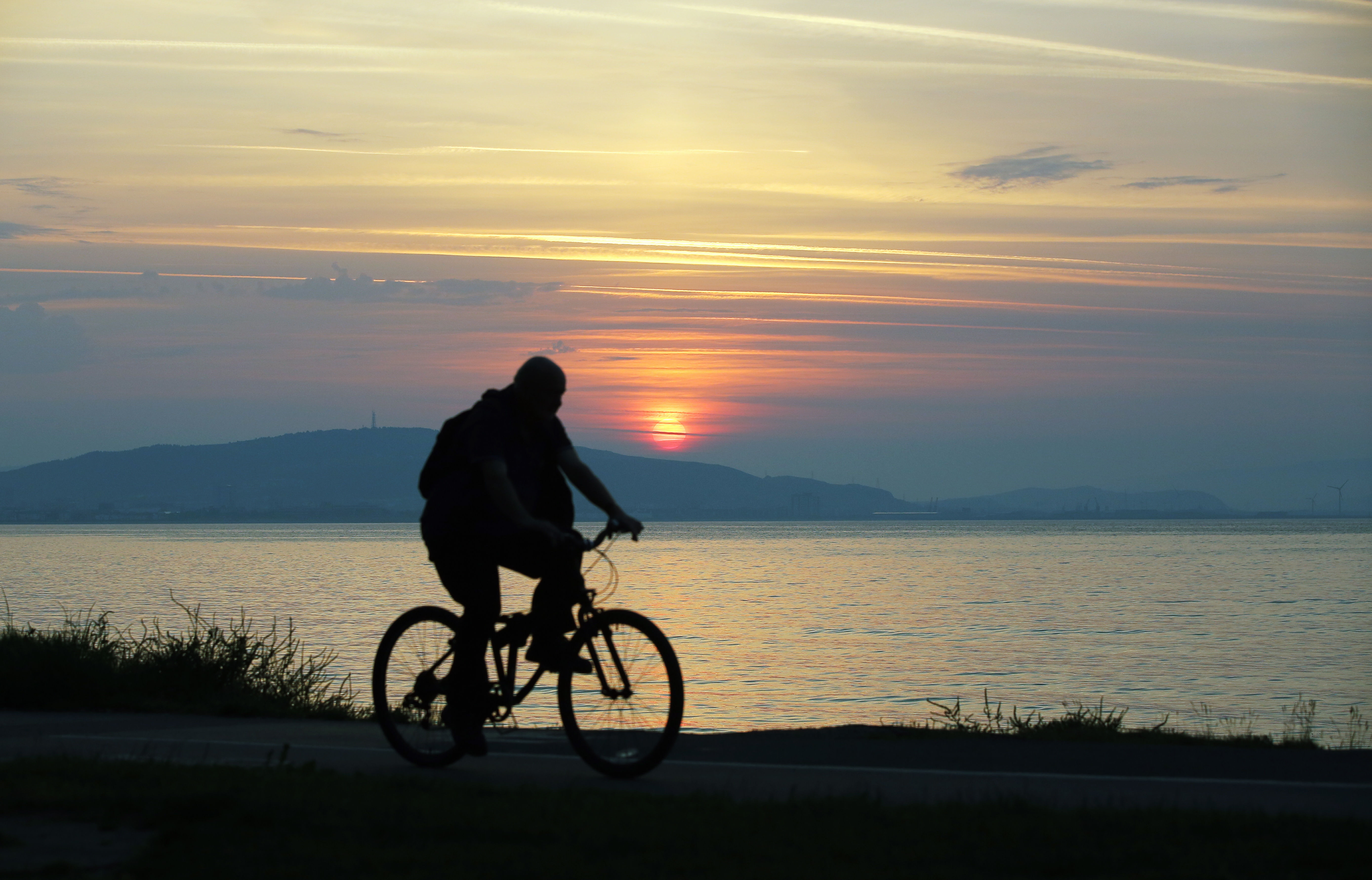 Pictured: A cyclist travels on the Oystermouth path as the sun rises over Kilvey Hill in Swansea, as seen from West Cross in south Wales, UK. Wednesday 21 June 2017 Re: Summer Solstice